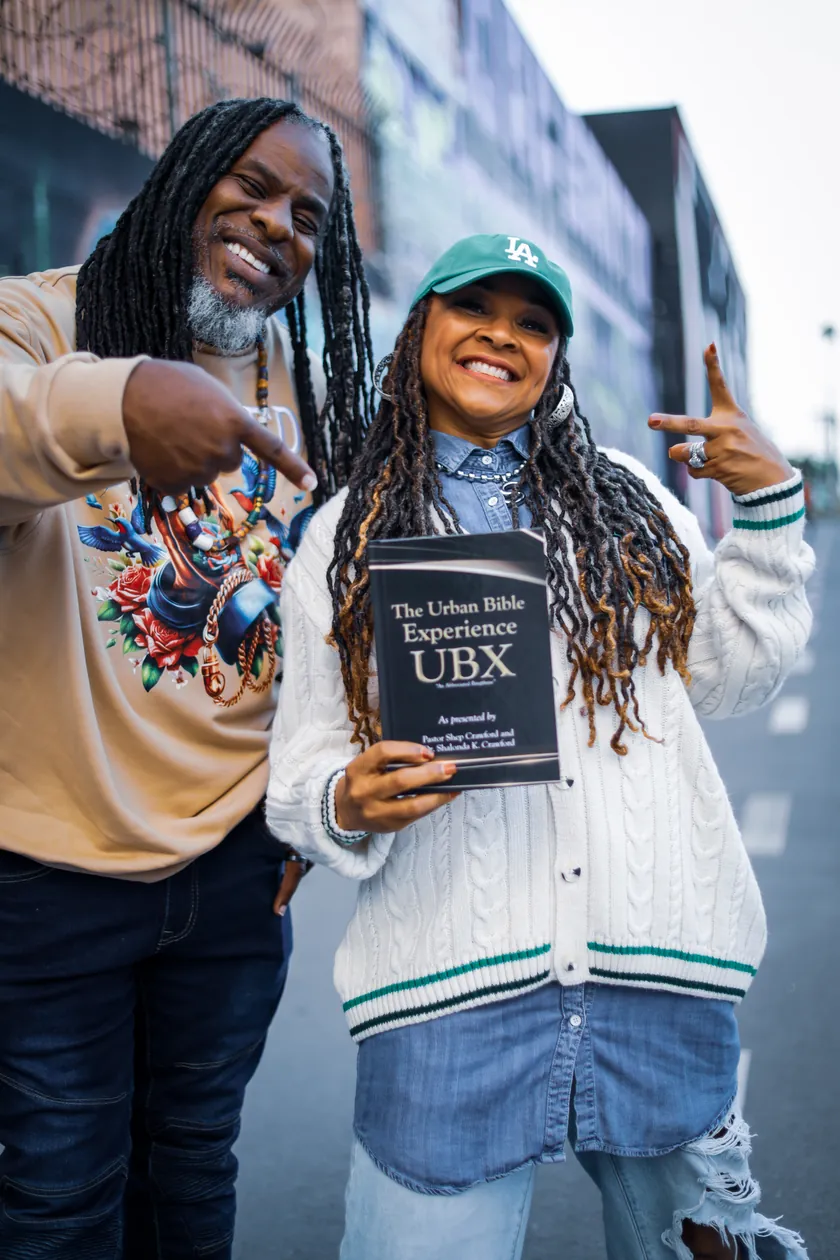 Pastor Shep and Dr. Sunshine together on a city street, holding The Urban Bible Experience book