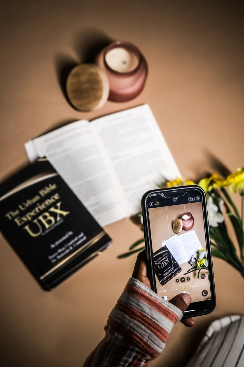 The Urban Bible Experience book beside an open Bible, with a hand photographing them on a smartphone